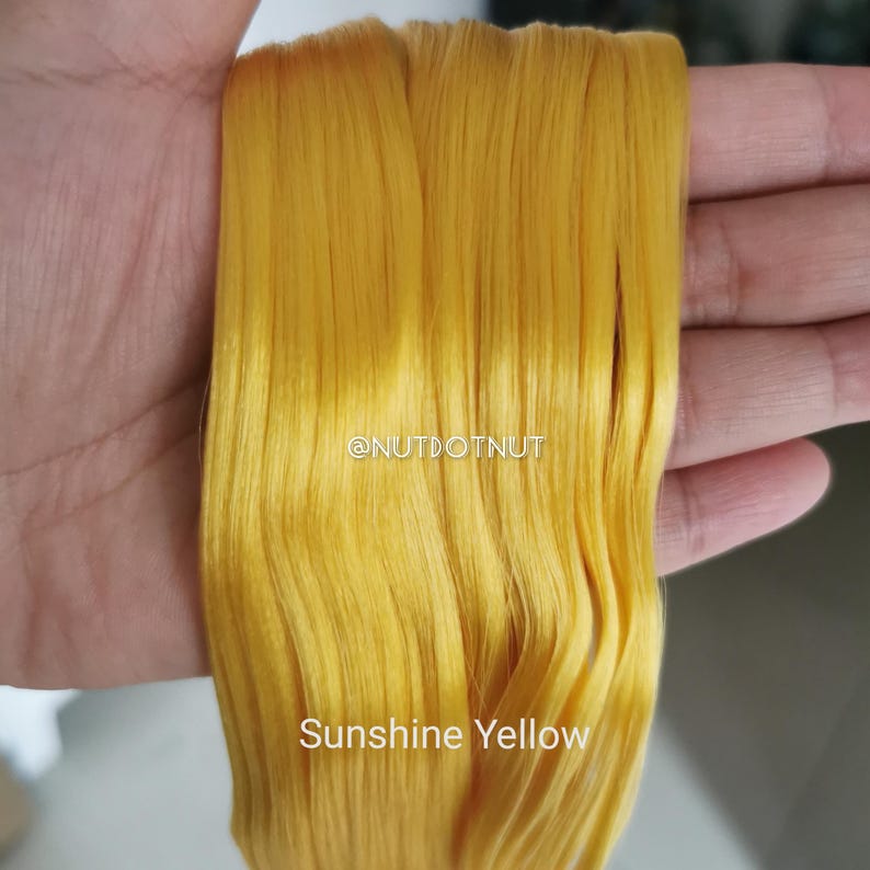 May include: A bundle of straight, vibrant sunshine yellow synthetic hair extensions. The text @NUTDOTNUT is printed in white in the center, and the words Sunshine Yellow are printed in white at the bottom of the yellow hair strands.