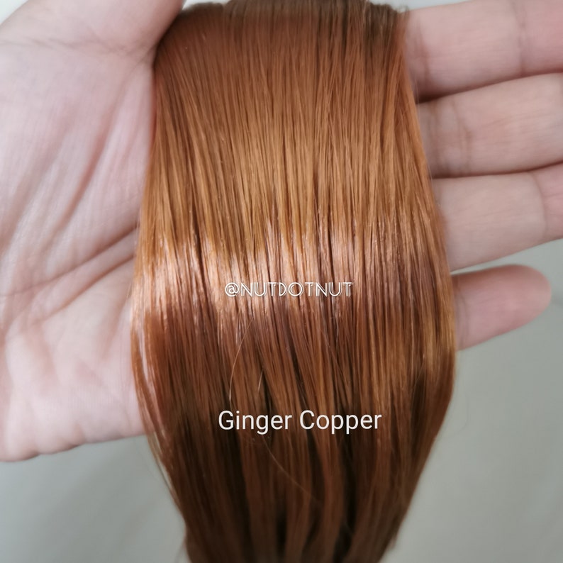 May include: A close-up of a strand of ginger copper coloured human hair extensions. The hair is smooth and shiny, and the colour is a warm, reddish-brown.