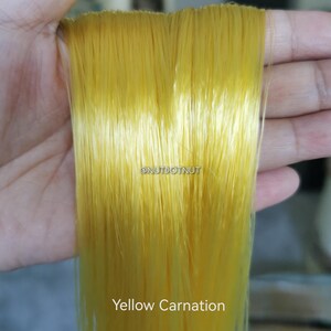 May include: A bundle of thin, straight, bright yellow synthetic fibers with a glossy finish. The text @NUTDOTNUT is printed in the center, and the text Yellow Carnation is printed at the bottom of the image, identifying the color of the fibers.