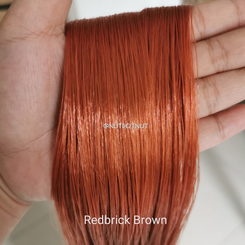 May include: A close-up of a strand of red-brown hair, showing the colour "Redbrick Brown". The hair is smooth and shiny, with a slight reddish tint.