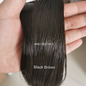 May include: Close-up of a dark brown human hair weft. The hair is smooth and shiny, with a slight wave. The text "Black Brown" is visible at the bottom of the image.