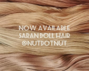 May include: Straight strands of synthetic doll hair in various shades of blonde and light brown are layered horizontally. The white text overlaid on the centre reads: NOW AVAILABLE SARAN DOLL HAIR @NUTDOTNUT.