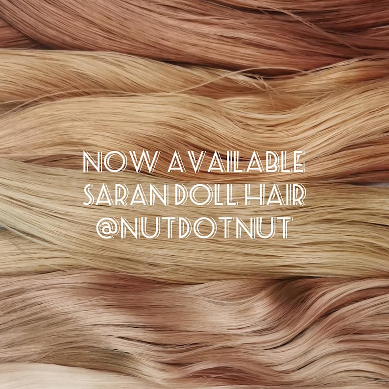 May include: Straight strands of synthetic doll hair in various shades of blonde and light brown are layered horizontally. The white text overlaid on the center reads: NOW AVAILABLE SARAN DOLL HAIR @NUTDOTNUT.