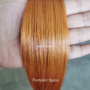 May include: Close-up of a strand of long, straight, orange-brown hair. The hair is smooth and shiny, with a warm, reddish-brown hue. The text "Pumpkin Spice" is visible at the bottom of the image.