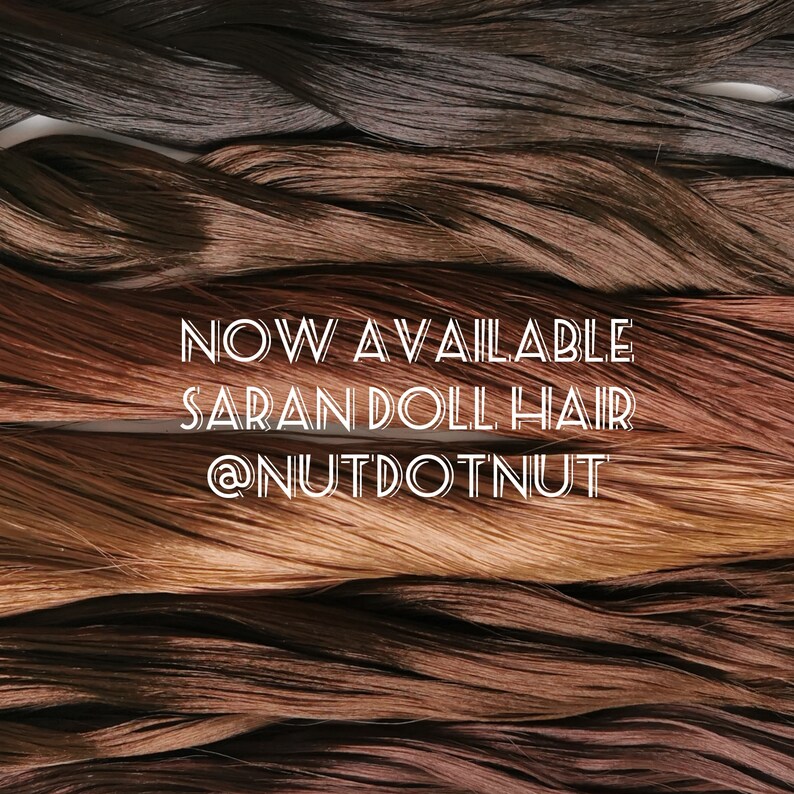 May include: A close-up of multiple strands of saran doll hair in various shades of brown. The text "NOW AVAILABLE SARAN DOLL HAIR @NUTDOTNUT" is superimposed on the image.
