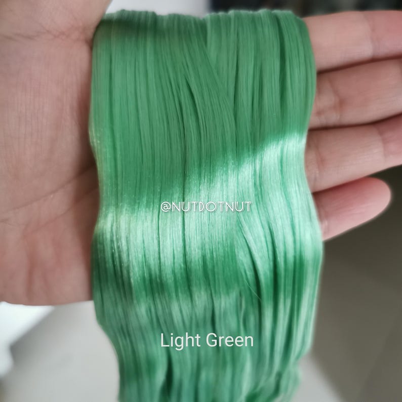 May include: A bundle of straight, light green synthetic hair fibers with a smooth, glossy finish. The text @NUTDOTNUT is printed in white in the center, and the words Light Green are printed in white at the bottom of the green hair strands.