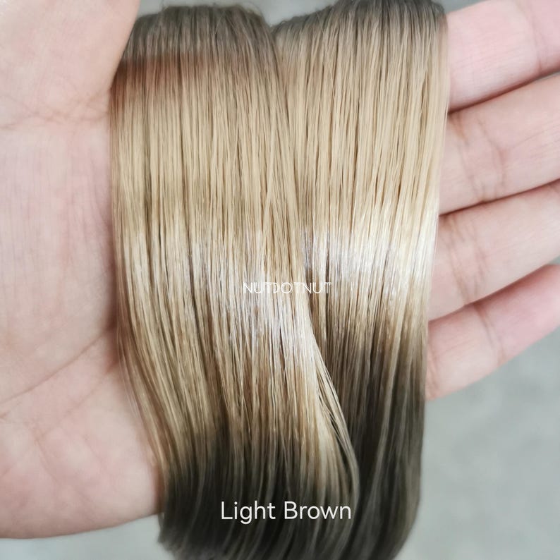May include: Two strands of straight hair extensions featuring a gradient color transition from a light blonde at the top to a dark brown at the bottom. The text NUTDOTNUT is visible in the center, and the text Light Brown appears at the bottom.