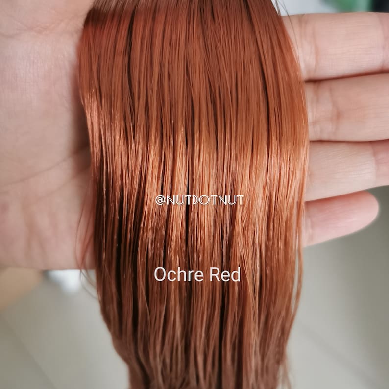 May include: A close-up of a strand of hair in a warm, reddish-brown colour called "Ochre Red". The hair is smooth and silky, with a slight sheen. The text "@nutdotnut" is visible in the image.