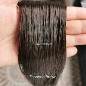 May include: Close-up of a bundle of dark brown human hair extensions. The hair is smooth and silky, with a slight sheen. The text "Espresso Brown" is visible at the bottom of the image.
