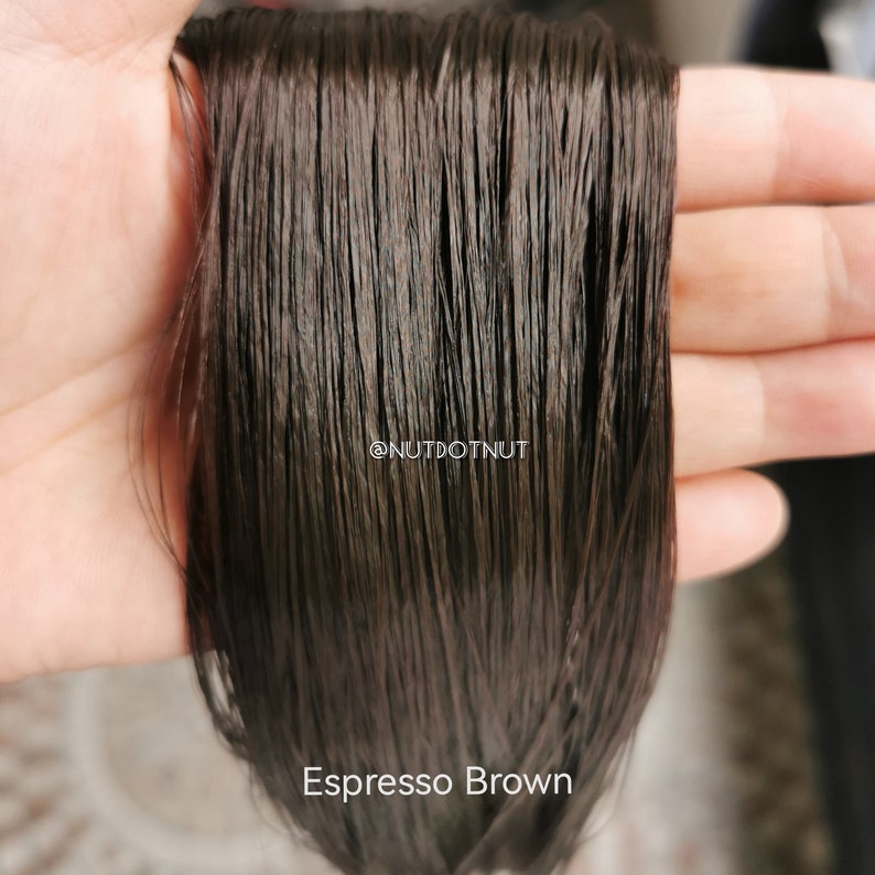 May include: Close-up of a bundle of dark brown human hair extensions. The hair is smooth and silky, with a slight sheen. The text "Espresso Brown" is visible at the bottom of the image.