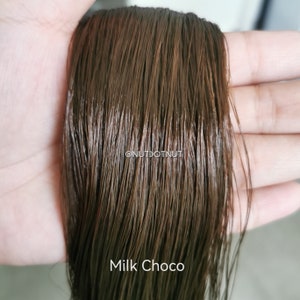 May include: A close-up of a strand of brown hair, showing the texture and color. The hair is labeled "Milk Choco".