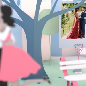 May include: A papercraft scene with a couple in a park. A photo of a couple in traditional Indian clothing is displayed on a stand with a pink heart. A bench with pink accents is in the foreground.