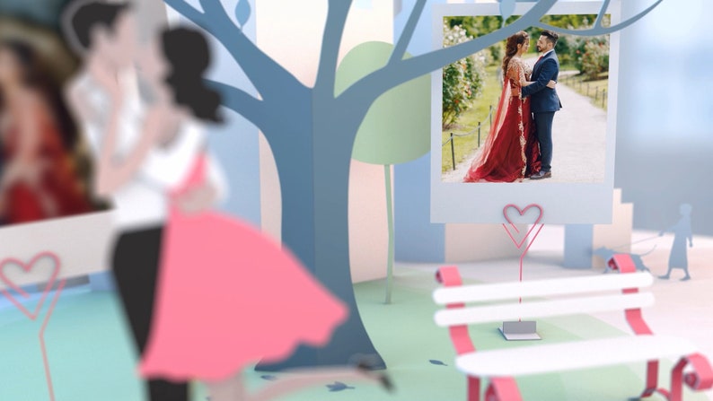 May include: A papercraft scene with a couple in a park. A photo of a couple in traditional Indian clothing is displayed on a stand with a pink heart. A bench with pink accents is in the foreground.