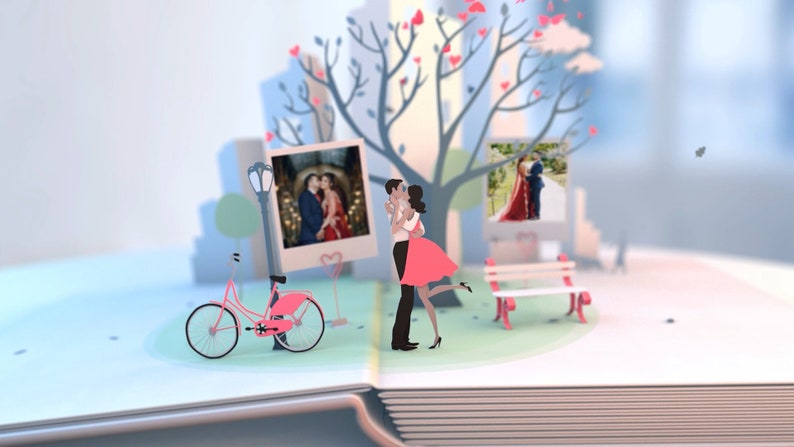May include: A pop-up book with a papercraft scene of a couple kissing under a tree with pink hearts. There is a pink bicycle, a bench, and three instant photos of the couple.