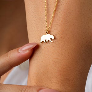May include: A gold chain necklace with a bear silhouette pendant.