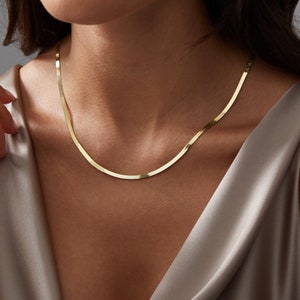 May include: A gold chain necklace with a snake chain design. The chain is thin and delicate, and it is worn by a person with a light brown complexion.