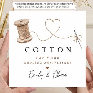 May include: A square greeting card featuring a flat printed design of a wooden spool with brown thread forming a heart shape, connected to a silver needle. The text reads: This is a flat printed design. All textures and decorative effects are printed, not real 3D embellishments. COTTON HAPPY 2ND WEDDING ANNIVERSARY Emily & Oliver.
