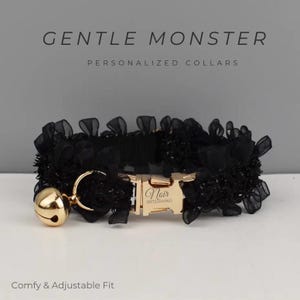 Könnte beinhalten: Schwarzes Haustierhalsband mit goldfarbener Schnalle und Glocke. Das Halsband ist mit schwarzer Spitze verziert und trägt den Namen "Noir" auf der Schnalle. Der Text "GENTLE MONSTER PERSONALIZED COLLARS" steht oben und "Comfy & Adjustable Fit" unten.