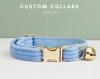 May include: A light blue cat collar with a gold buckle and a bell. The collar is made of a soft, velvety material. The text "CUSTOM COLLARS BABYCAT" is displayed above the collar.