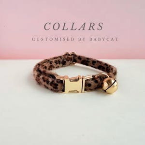 Puede incluir: Un collar para gato con estampado de leopardo, hebilla dorada y una pequeña campana dorada. El texto "COLLARS" y "CUSTOMISED BY BABYCAT" es visible en el fondo.