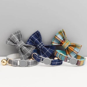 Puede incluir: Tres collares para gatos con pajaritas a cuadros. Los collares son grises, azul marino y turquesa. Cada collar tiene un cierre de plástico gris y una campana dorada.