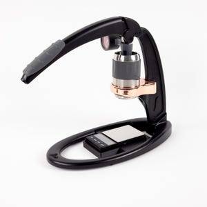 以下が含まれることがあります： 銅色のアクセントと内蔵スケールを備えた黒色の手動エスプレッソメーカー。レバーハンドルにはグレーのグリップが付いています。ベースは楕円形です。家庭での使用向けに設計されています。