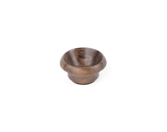May include: A small, wooden bowl with a dark brown finish. The bowl is round and has a slightly flared lip.