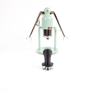 May include: A mint green espresso machine with a chrome finish and a black tamper. The machine has a lever on the side and a gauge on the front.