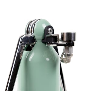 May include: A close-up of a green and chrome espresso machine with a chrome steam wand and a chrome pressure gauge.