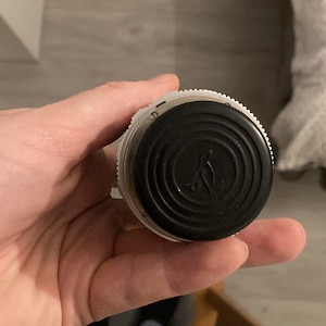 Op de afbeelding: Een zwarte en witte flessenstop met een cirkelvormig ontwerp en een klein vogellogo. De stop is gemaakt van plastic en heeft een getextureerd oppervlak.