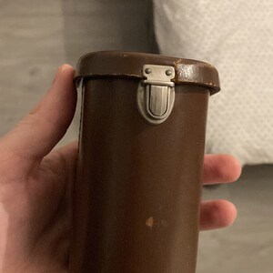 May include: A brown leather camera case with a silver metal latch.