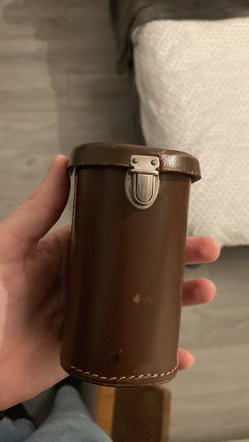 May include: A brown leather camera case with a silver metal latch.