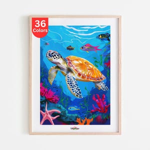 Op de afbeelding: Een ingelijste print met een onderwaterlandschap. Een zeeschildpad met een oranje schild en patronen op de vinnen zwemt tussen kleurrijk koraal en vissen. De print bevat de tekst "36 Colors" in een rode cirkel.