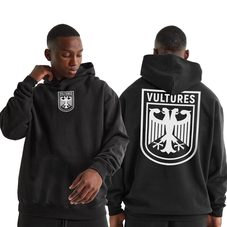 K&ouml;nnte beinhalten: Schwarzer Kapuzenpullover mit einem wei&szlig;en Adlerwappen und dem Wort "VULTURES" auf der R&uuml;ckseite. Das Adlerwappen befindet sich auch auf der Vorderseite des Pullovers.