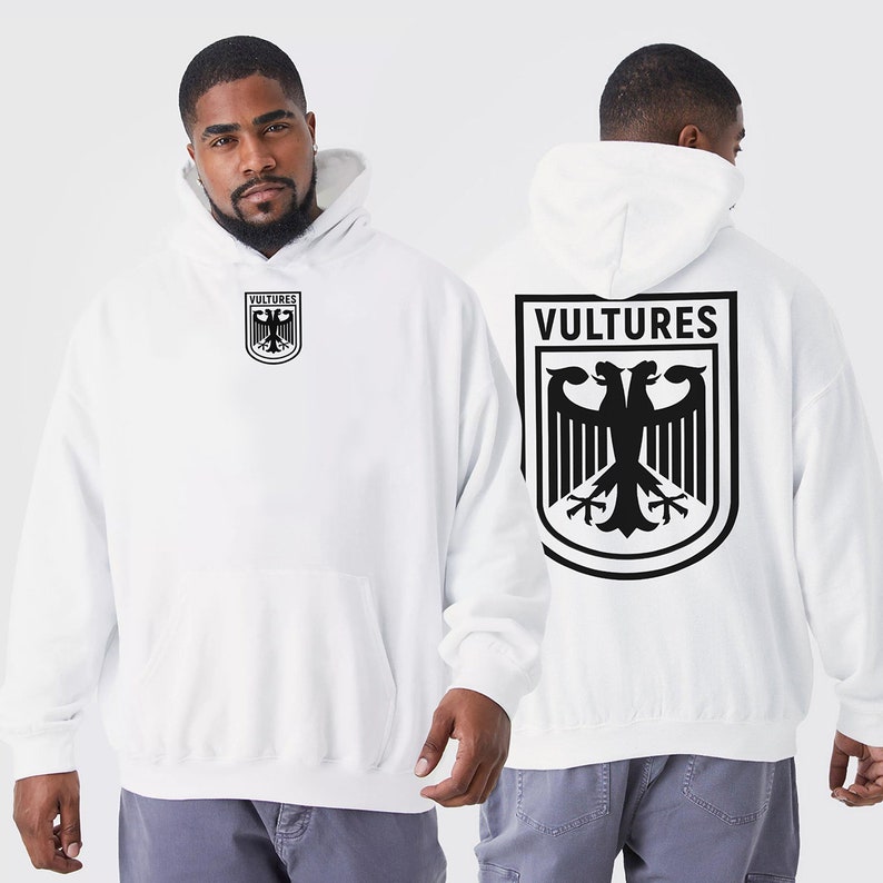 K&ouml;nnte beinhalten: Wei&szlig;er Kapuzenpullover mit einem schwarzen Adler-Motiv und dem Wort "VULTURES" auf der R&uuml;ckseite. Die Vorderseite des Pullovers hat eine kleinere Version des Adler-Motivs mit dem Wort "VULTURES" darunter.