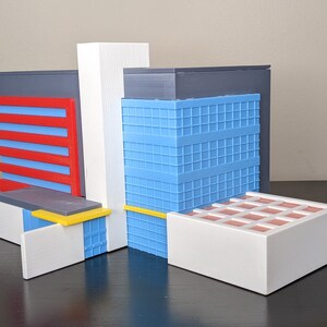 May include: A 3D printed model of a modern building with a blue, red, white and yellow colour scheme. The building has a flat roof and a variety of windows and doors.