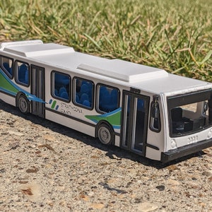 Peut inclure: Bus jouet blanc avec des accents bleus et verts. Le bus indique "Strathcona County" sur le côté.