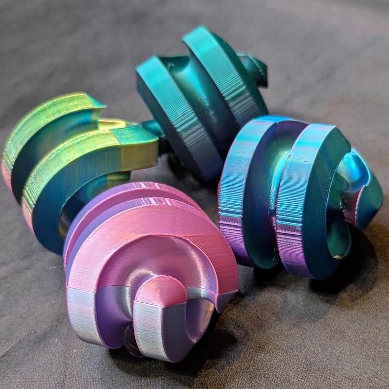 May include: Four iridescent, spiral-shaped objects in shades of teal, purple, and gold. The objects have a textured, ridged surface and a rounded, curved shape. The objects are arranged in a cluster, with a dark background.