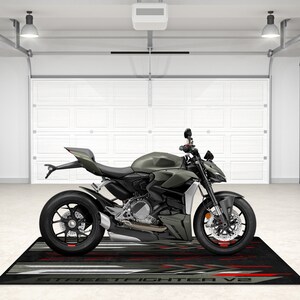 Puede incluir: Una motocicleta verde con ruedas negras y un asiento negro. La motocicleta est&aacute; aparcada en un garaje con una puerta de garaje blanca y una alfombra negra con las palabras "STREETFIGHTER V2" impresas en ella.