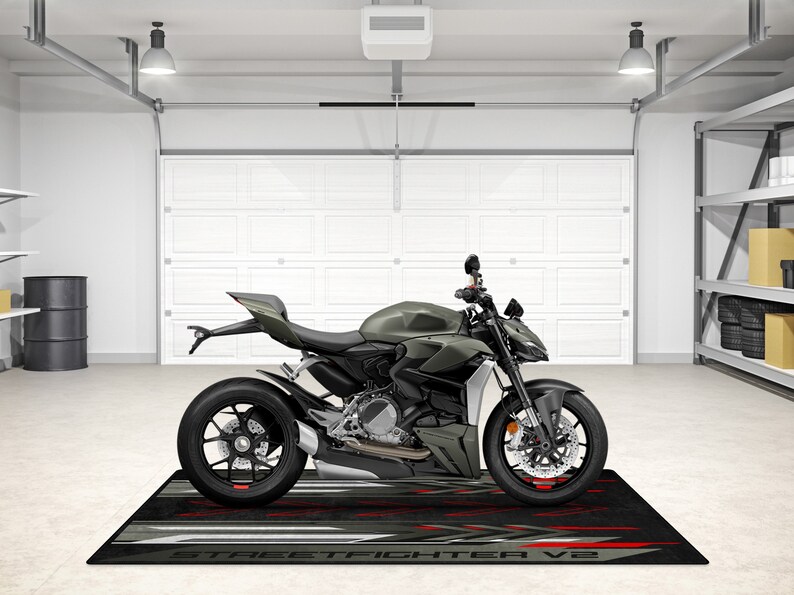 Puede incluir: Una motocicleta verde con ruedas negras y un asiento negro. La motocicleta est&aacute; aparcada en un garaje con una puerta de garaje blanca y una alfombra negra con las palabras "STREETFIGHTER V2" impresas en ella.