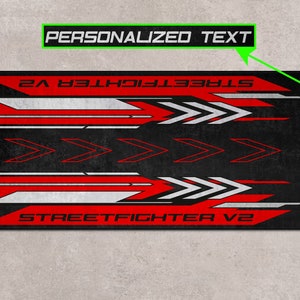 Puede incluir: Alfombrilla de rat&oacute;n para juegos negra y roja con detalles blancos y el texto "STREET FIGHTER V2" y "TEXTO PERSONALIZADO".