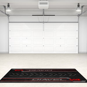 Op de afbeelding: Zwarte garagevloermat met rode en grijze accenten. De mat heeft de tekst "Diavel V4" en een reeks pijlen die naar rechts wijzen.
