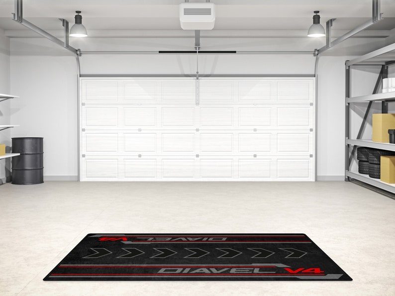 Op de afbeelding: Zwarte garagevloermat met rode en grijze accenten. De mat heeft de tekst "Diavel V4" en een reeks pijlen die naar rechts wijzen.