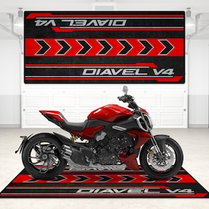 Op de afbeelding: Een rode Ducati Diavel V4 motorfiets geparkeerd op een zwart en rode garagevloermat met de woorden "Diavel V4" erop gedrukt.