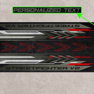 Puede incluir: Alfombrilla de rat&oacute;n para juegos de color negro y gris con detalles rojos y el texto "STREET FIGHTER V2" y "TEXTO PERSONALIZADO".