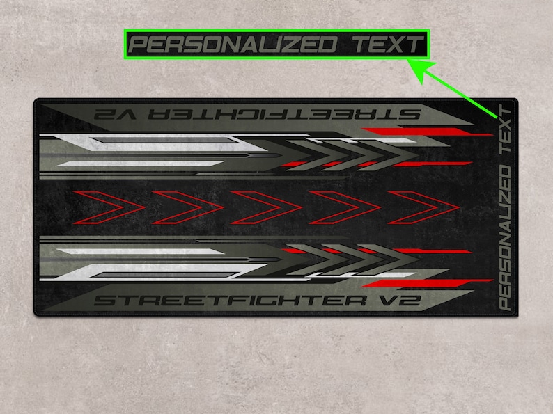 Puede incluir: Alfombrilla de rat&oacute;n para juegos de color negro y gris con detalles rojos y el texto "STREET FIGHTER V2" y "TEXTO PERSONALIZADO".