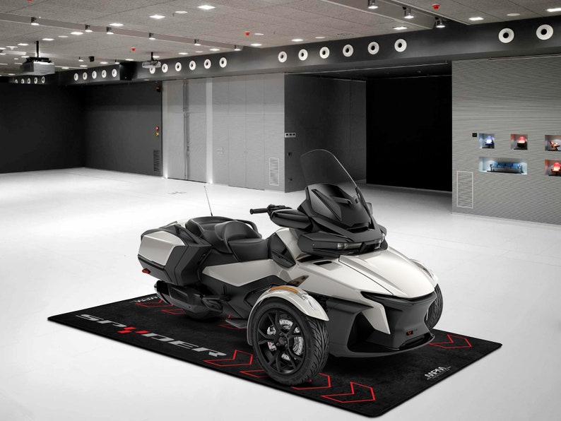 Op de afbeelding: Een wit-zwarte driewielige motorfiets met een zwarte voorruit en een zwarte stoel. De motorfiets staat op een zwarte mat met het woord "SPRINTER" in rood.