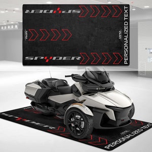 Op de afbeelding: Zwarte en rode motorfiets vloermat met het woord "SPIDER" in wit gedrukt. De mat heeft rode pijlen die naar rechts wijzen en de tekst "GEPERSONALISEERDE TEKST" gedrukt aan de rechterkant.