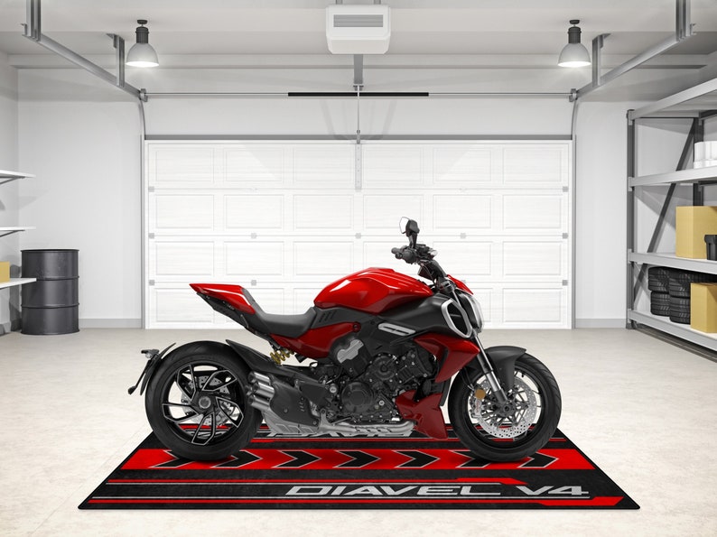 Op de afbeelding: Een rode Ducati Diavel V4 motorfiets geparkeerd in een garage op een zwart en rode motorfietsmat met de woorden "Diavel V4" erop gedrukt.