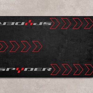 Op de afbeelding: Een zwarte muismat met rode pijlen en het woord "SPIDER" in grijze letters. De tekst "MPWM" staat aan de rechter- en linkerkant van de muismat.